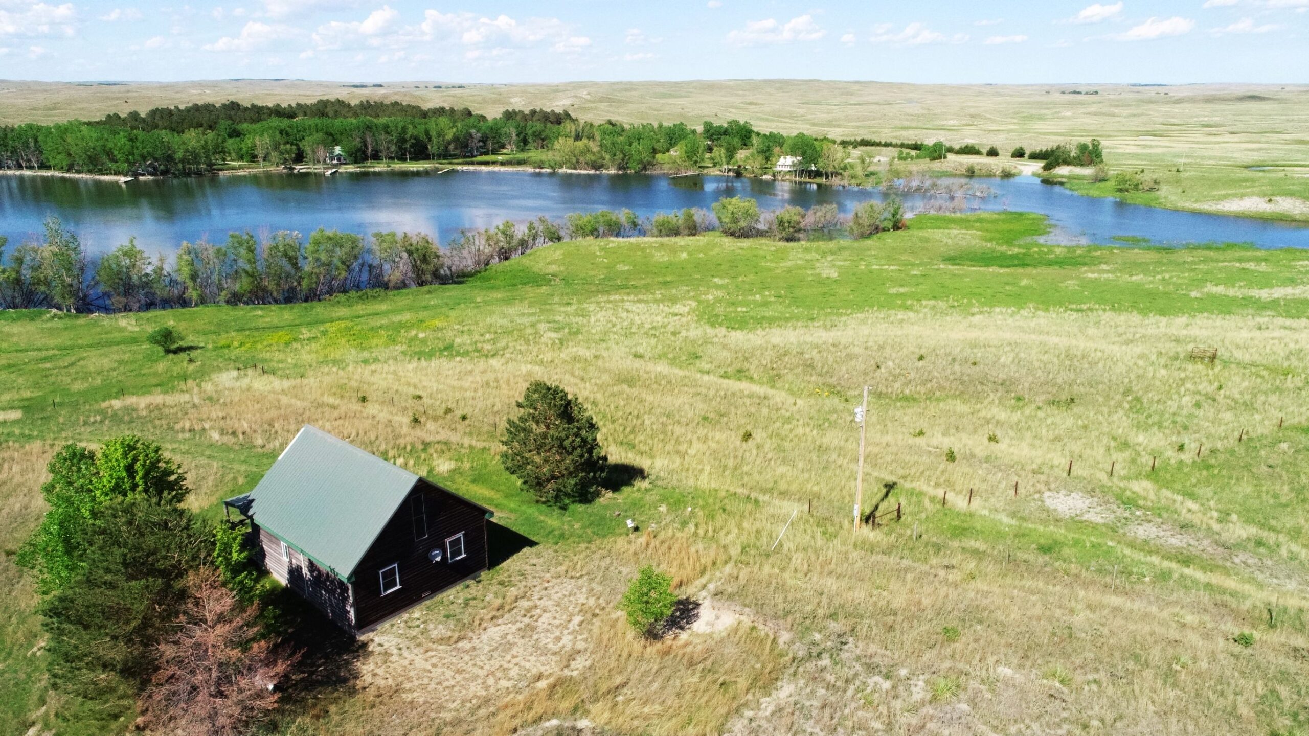 An image representing Nebraska Acreages for Sale listings by Lashley Land - a home sitting on the plains of Nebraska, with a small lake in the background.